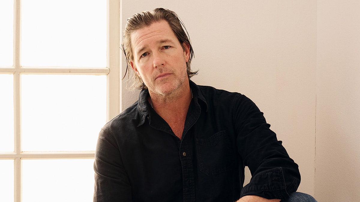 Ed Burns lleva una camisa oscura.