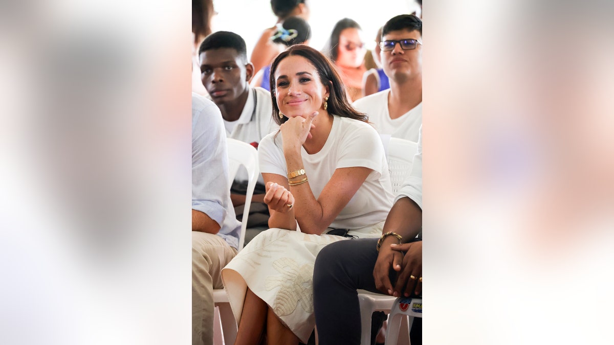 Meghan Markle smiling wearing all white sitting with an audience.