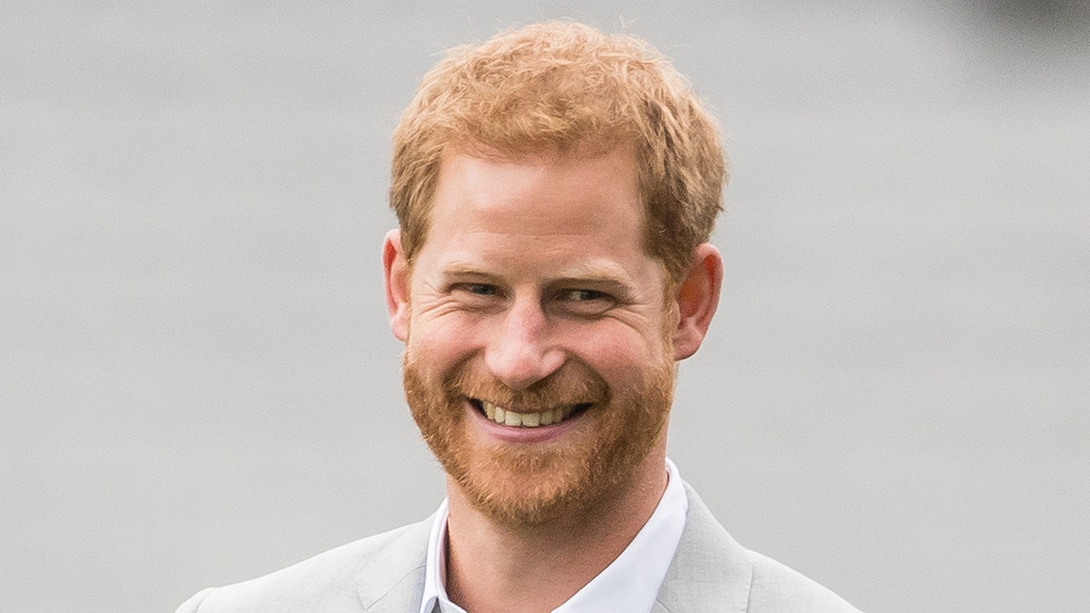 A close-up of Prince Harry smiling in a white suit.