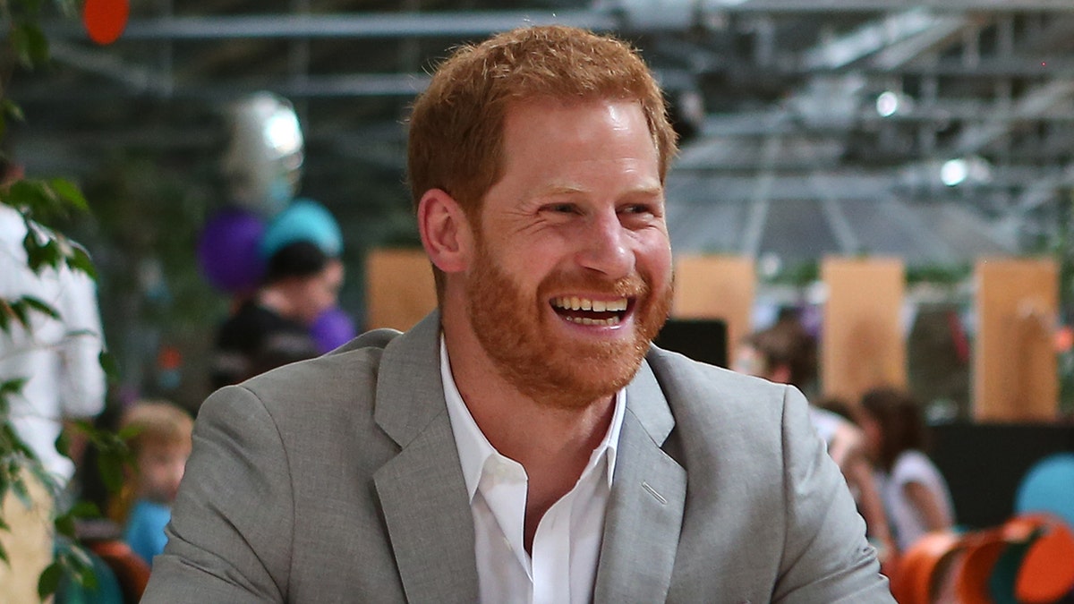 A close-up of Prince Harry smiling in a grey suit.