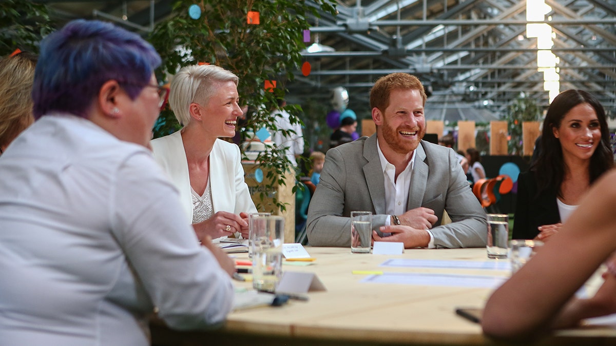 Prince Harry and Meghan Markle sitting next to each other as Prince Harry smiles