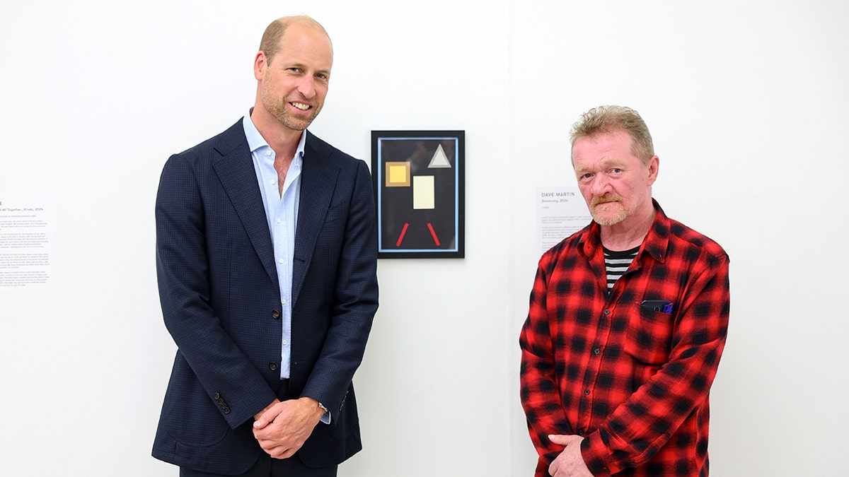 Prince William posing with a man wearing a red plaid shirt at an art gallery.