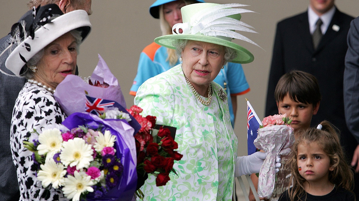 Queen Elizabeth handing a bouquet of flowers to her lady-in-waiting.