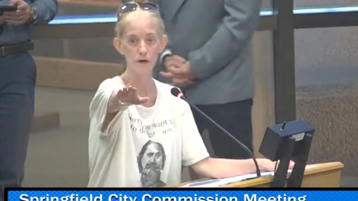 Woman in white t-shirt in front of microphone at a meeting