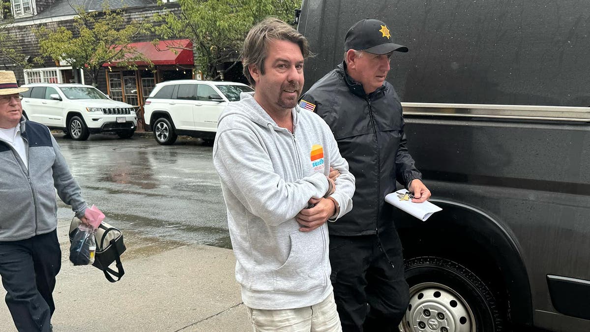 A erstwhile  advisor to John Kerry is handcuffed and wearing a grey hoodie arsenic  helium  is escorted by instrumentality    enforcement connected  a rainy day