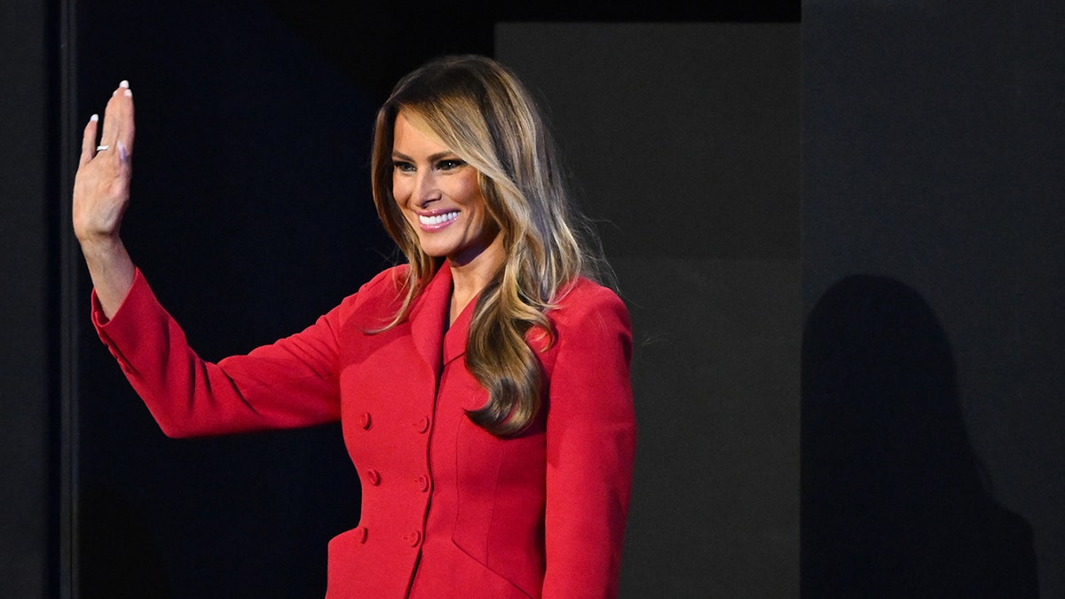 Melania Trump mengenakan setelan merah sambil melambaikan tangan