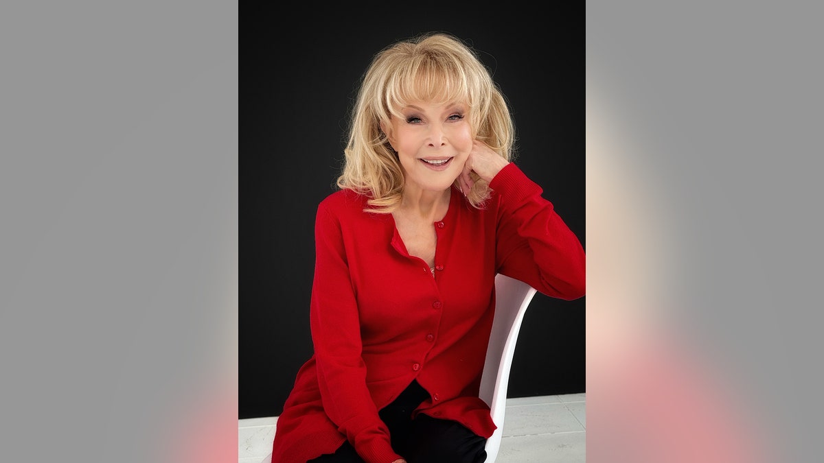 Barbara Eden wearing a red blouse and black pants.