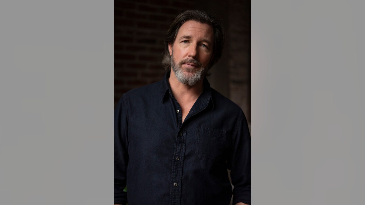 Ed Burns lleva una camisa oscura.