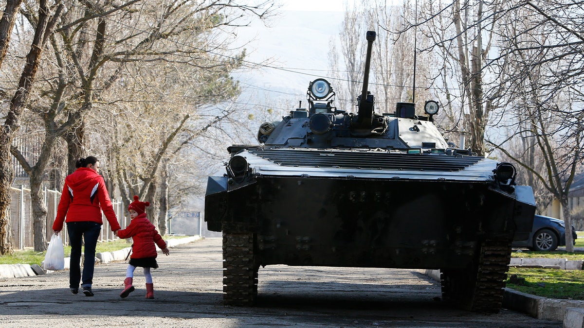 Uma mulher e uma criança passam por um veículo blindado em uma base militar em Perevalnoye, perto da cidade de Simferopol, na Crimeia, em 21 de março de 2014. 