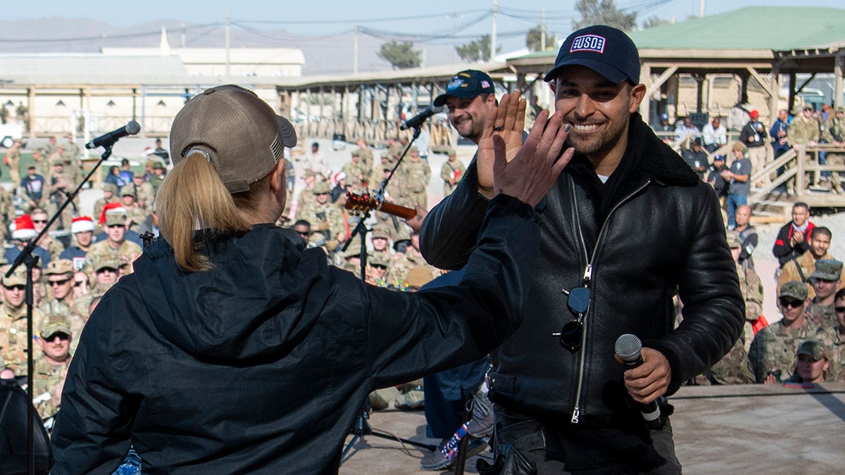 Wilmer Valderrama chocando los cinco con una mujer con gorra y chaqueta.