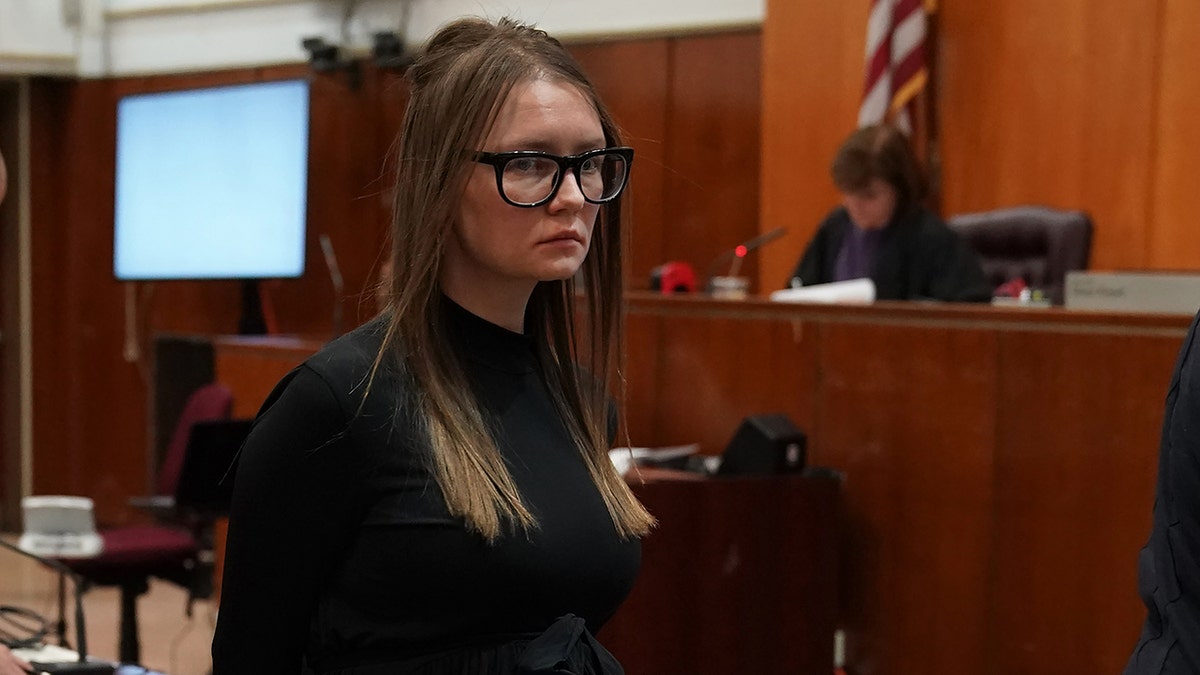 Anna 'Delvey' Sorokin in a black shirt and black framed glasses looks serious in court