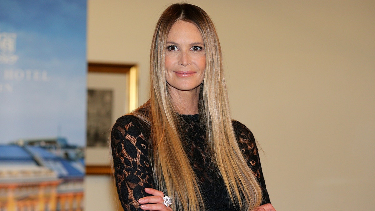 Elle Macpherson con un vestido negro de encaje sonríe suavemente mientras cruza los brazos