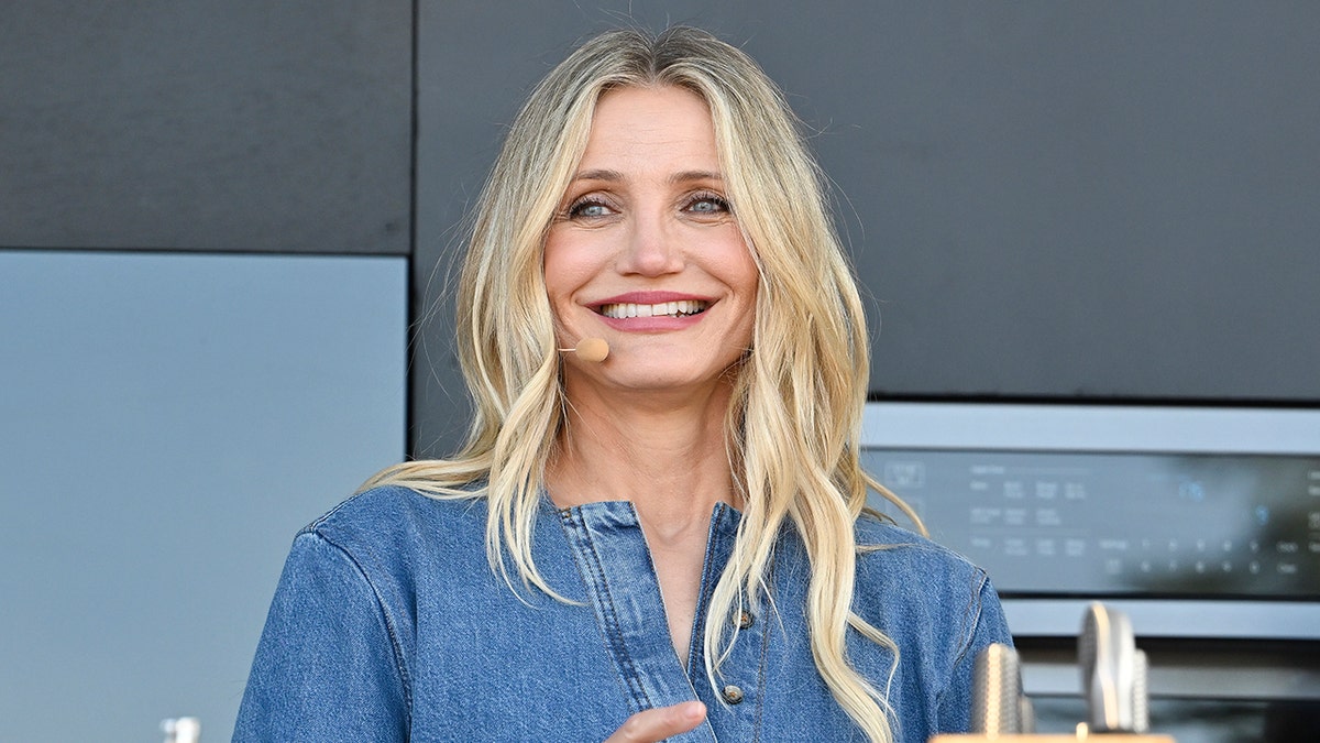 Cameron Diaz in a denim shirt smiles on stage with a skin-colored headpiece attached to her