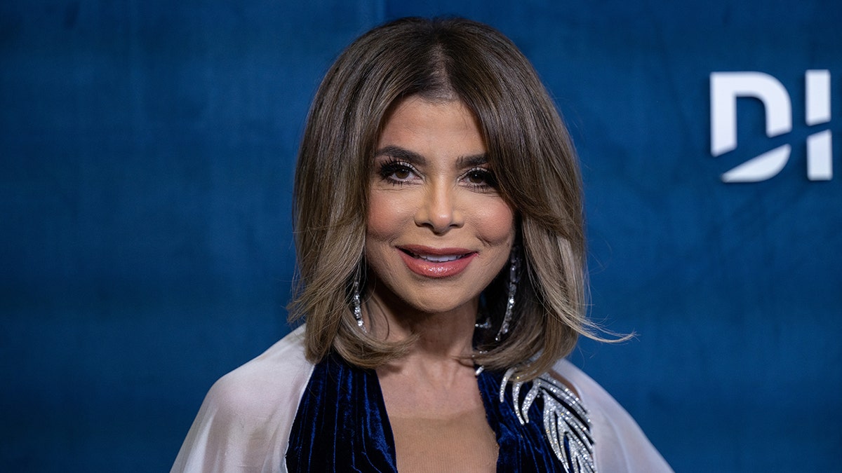 Paula Abdul smiles directly into the camera in a blue dress and a white scarf