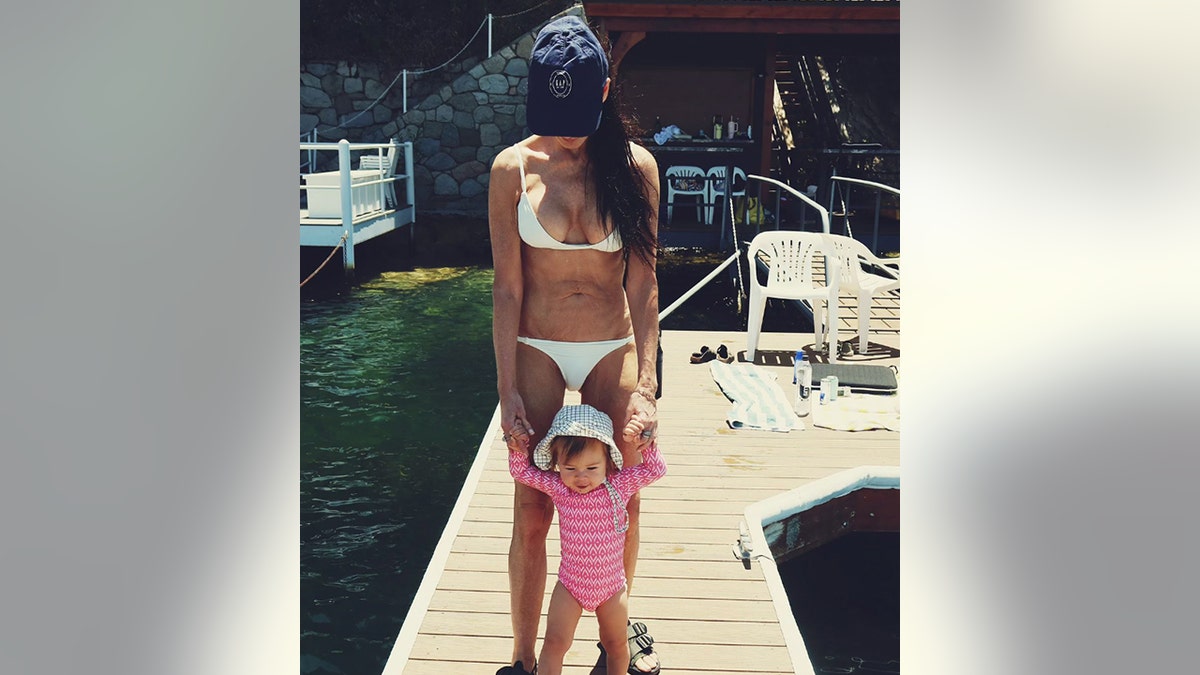 Demi Moore in a white bikini and hat holds the hands of her granddaughter Louetta while walking on a dock