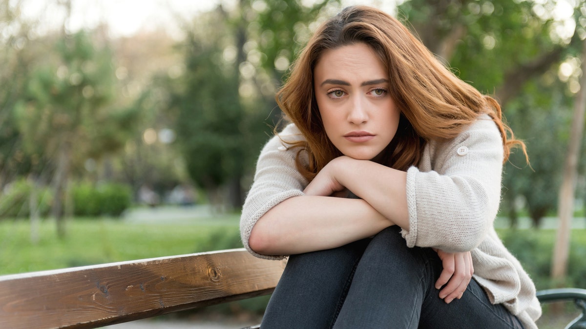 A sad woman sitting on a bench outside.