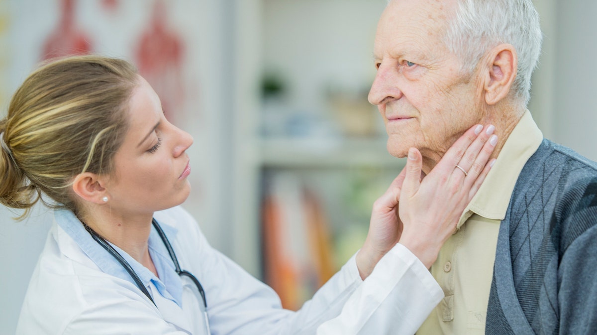 Doctor examinando la glándula tiroides de un anciano