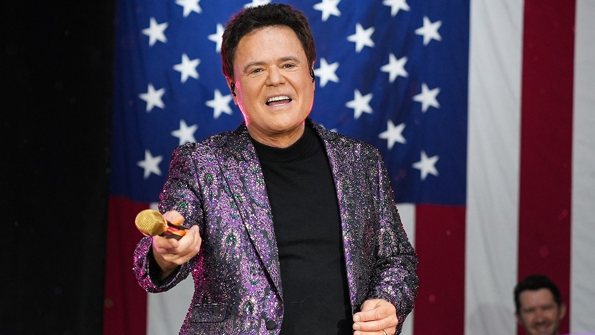 Donny Osmond performing on stage in front of an American flag.