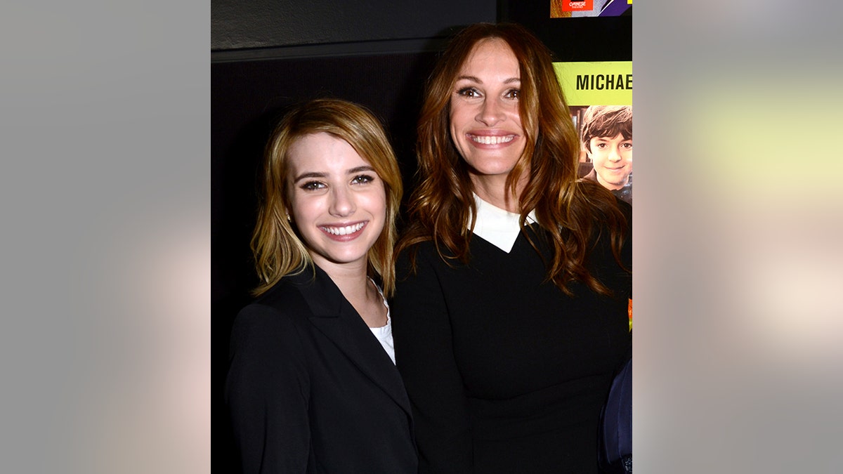 Emma Roberts in a black jacket laughs with aunt Julia Roberts in a black sweater over a white shirt