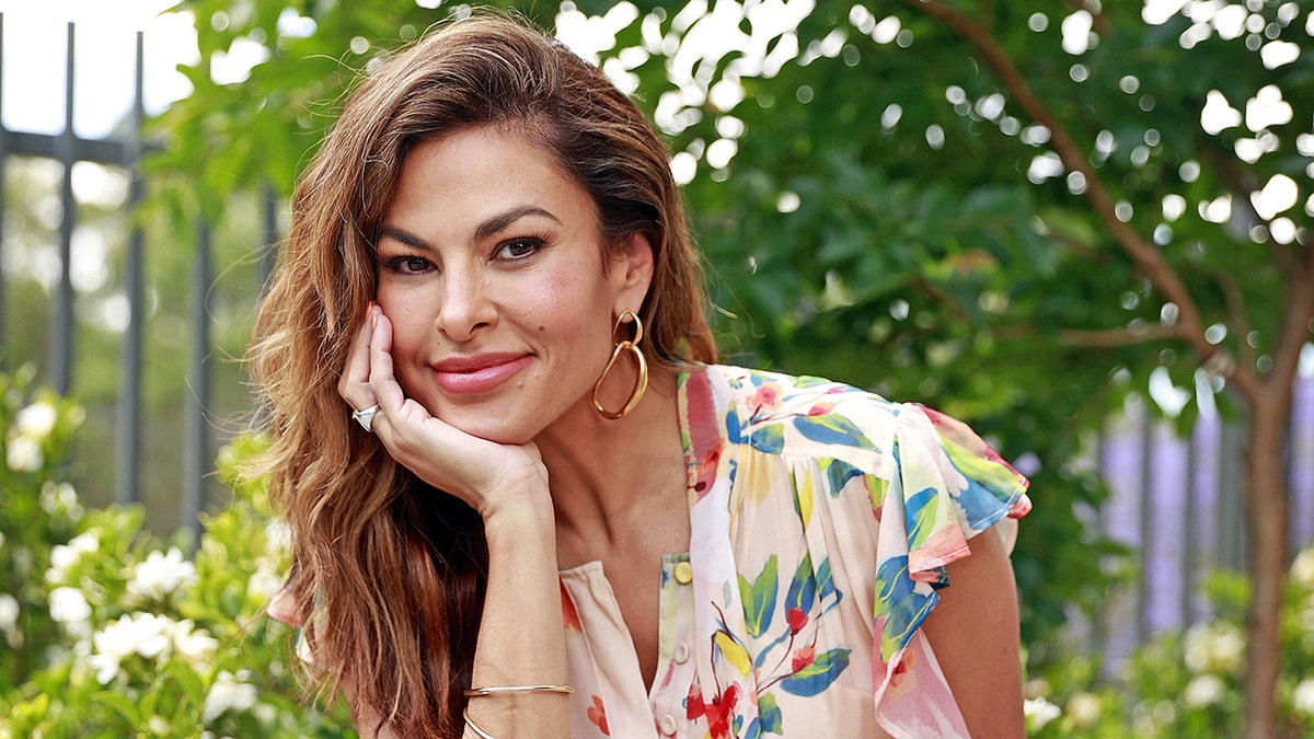 Eva Mendes soft smiles in a light pink dress with flowers as she rests her hand <a target=