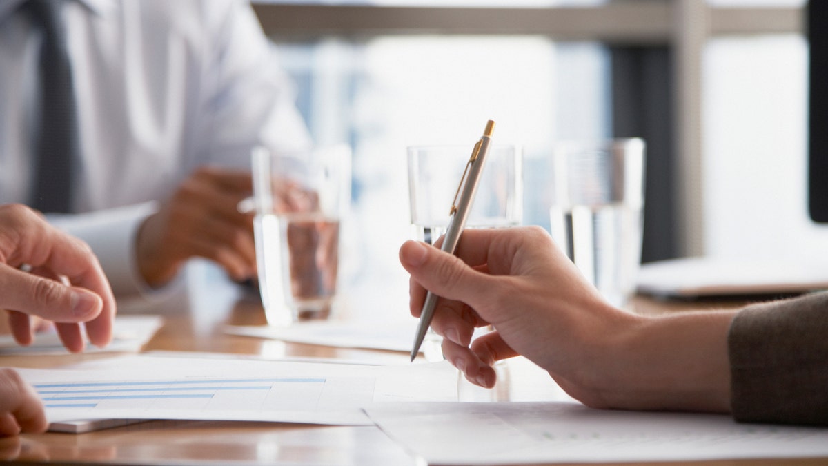 Executives sit with glasses of water at a boardroom table.