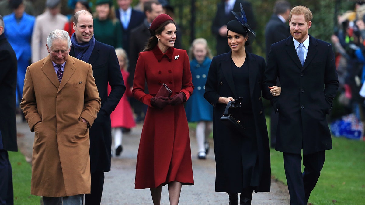 El rey Carlos, con un abrigo color canela, camina delante del príncipe Guillermo y al lado de Kate Middleton, con una chaqueta roja, junto a Meghan Markle y el príncipe Harry