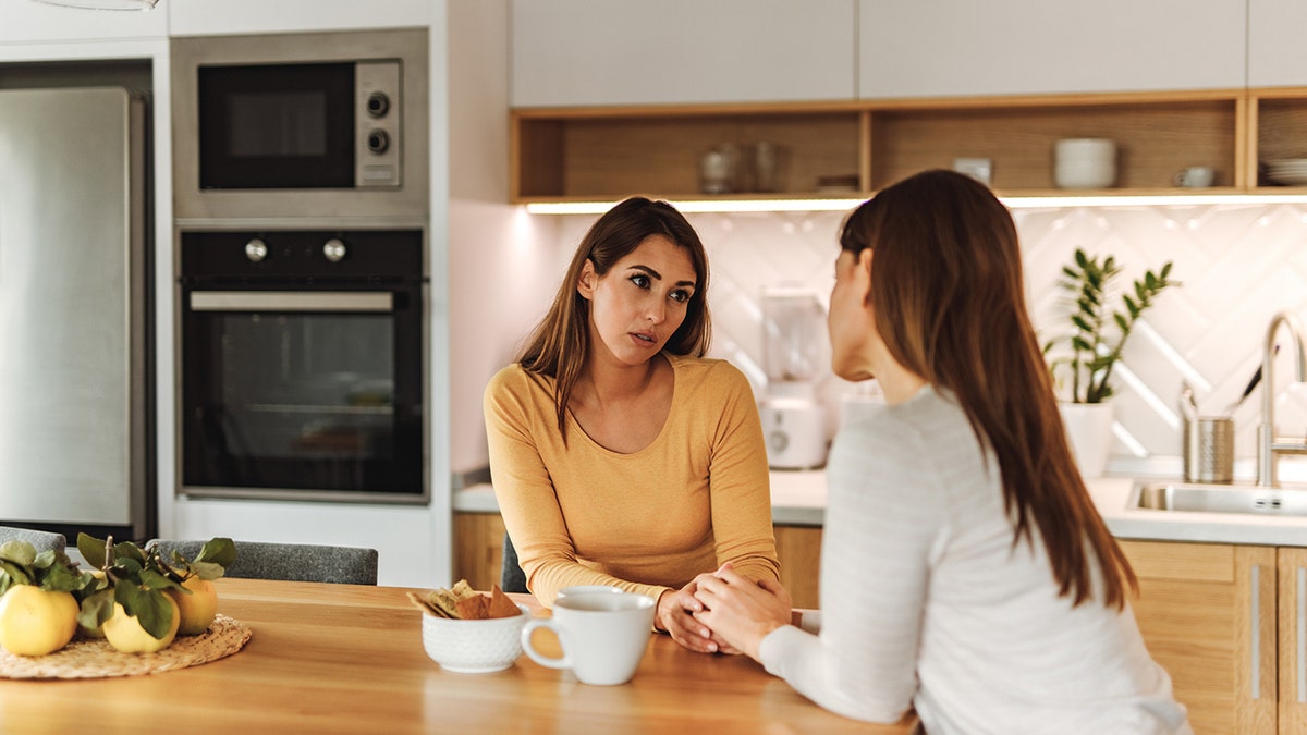 Two women are talking in a kitchen.