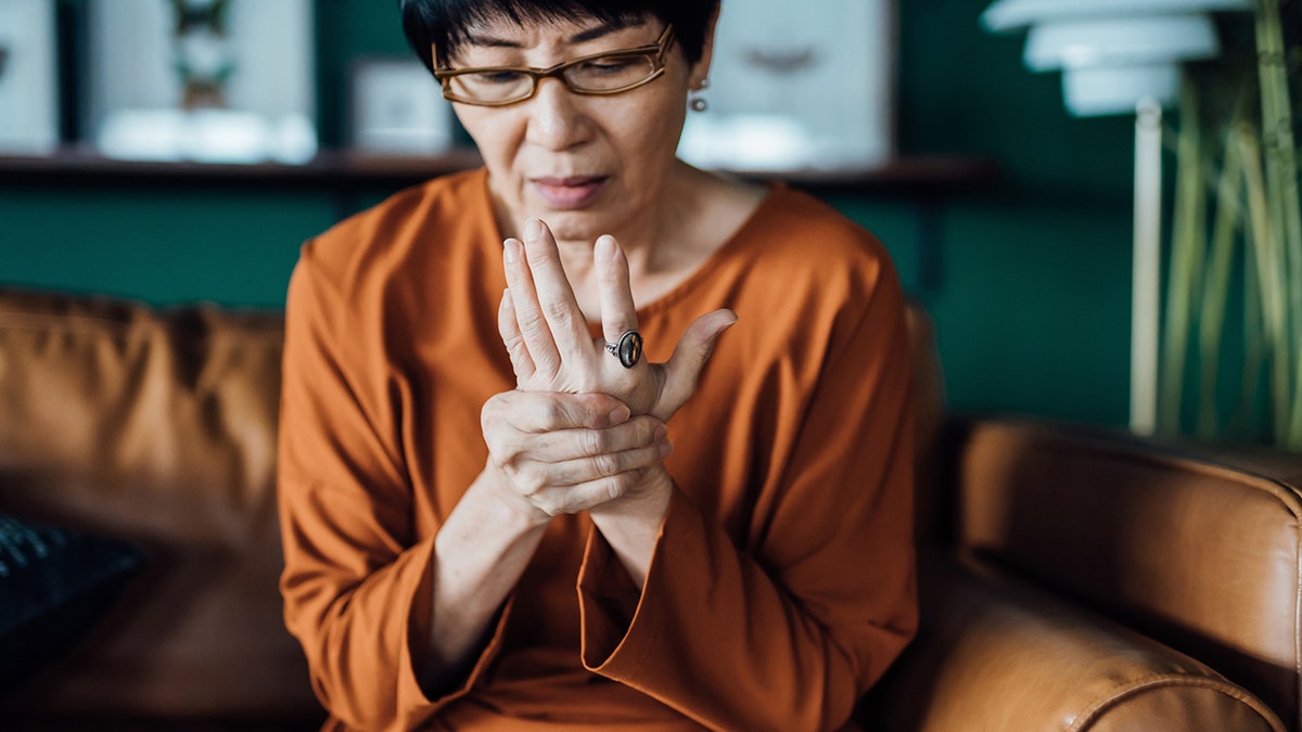 woman rubbing her hands in discomfort, suffering from arthritis while sitting on sofa