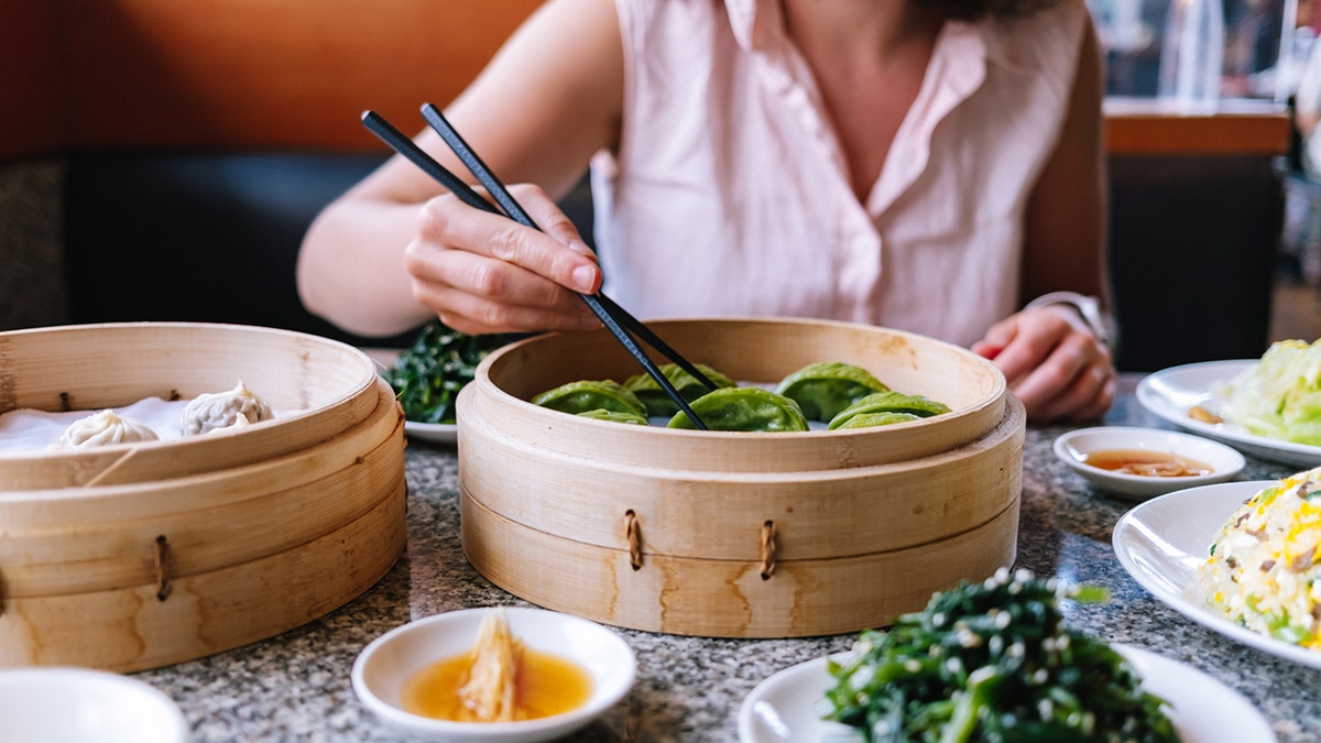 Mujer comiendo dumplings y otros alimentos asiáticos con palillos.