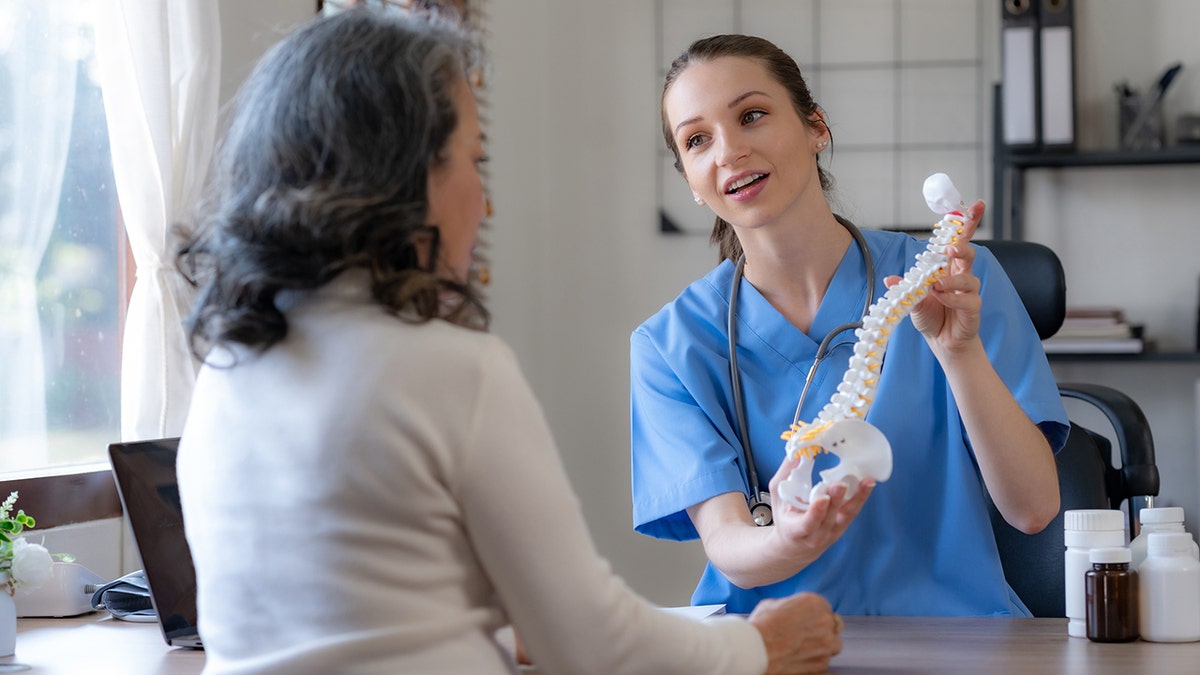 un médico muestra a una paciente el modelo de una columna vertebral humana