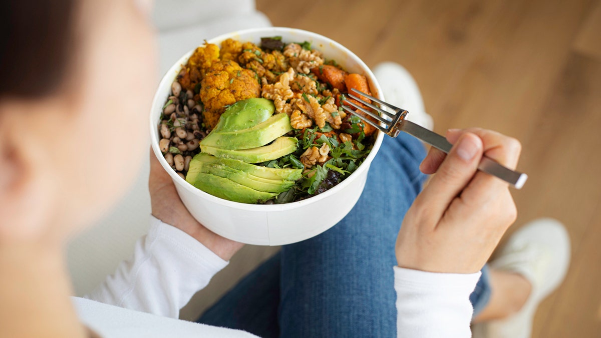 Mujer comiendo ensalada fresca, aguacate, judías y verduras.