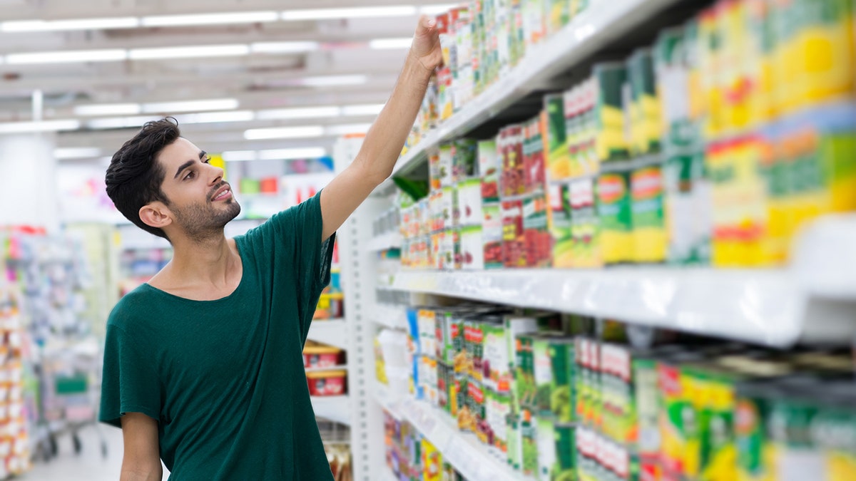 Jóvenes clientes que toman comida enlatada del estante de la tienda.