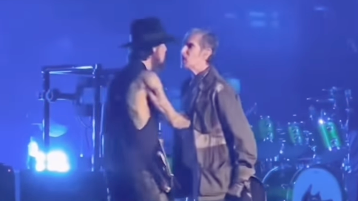 Dave Navarro, parcialmente de espaldas a la cámara, mantiene un acalorado intercambio con Perry Farrell, miembro de la banda, que se inclina hacia Dave