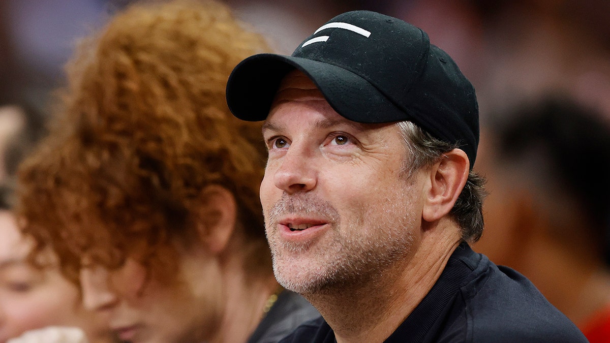 Jason Sudeikis looks up in a black shirt and cap while attending the WNBA All Star game