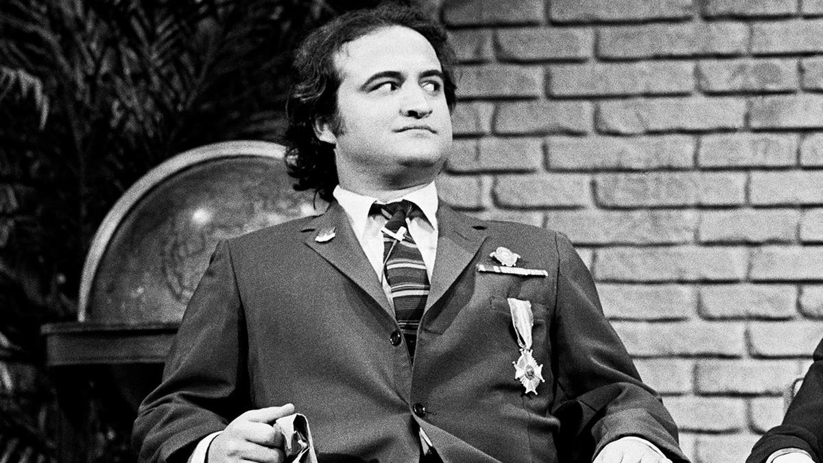 John Belushi in a suit looking serious on the set of Saturday Night Live