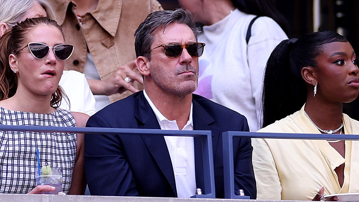 Jon Hamm in a blue blazer and sunglasses watches the US Open final seriously