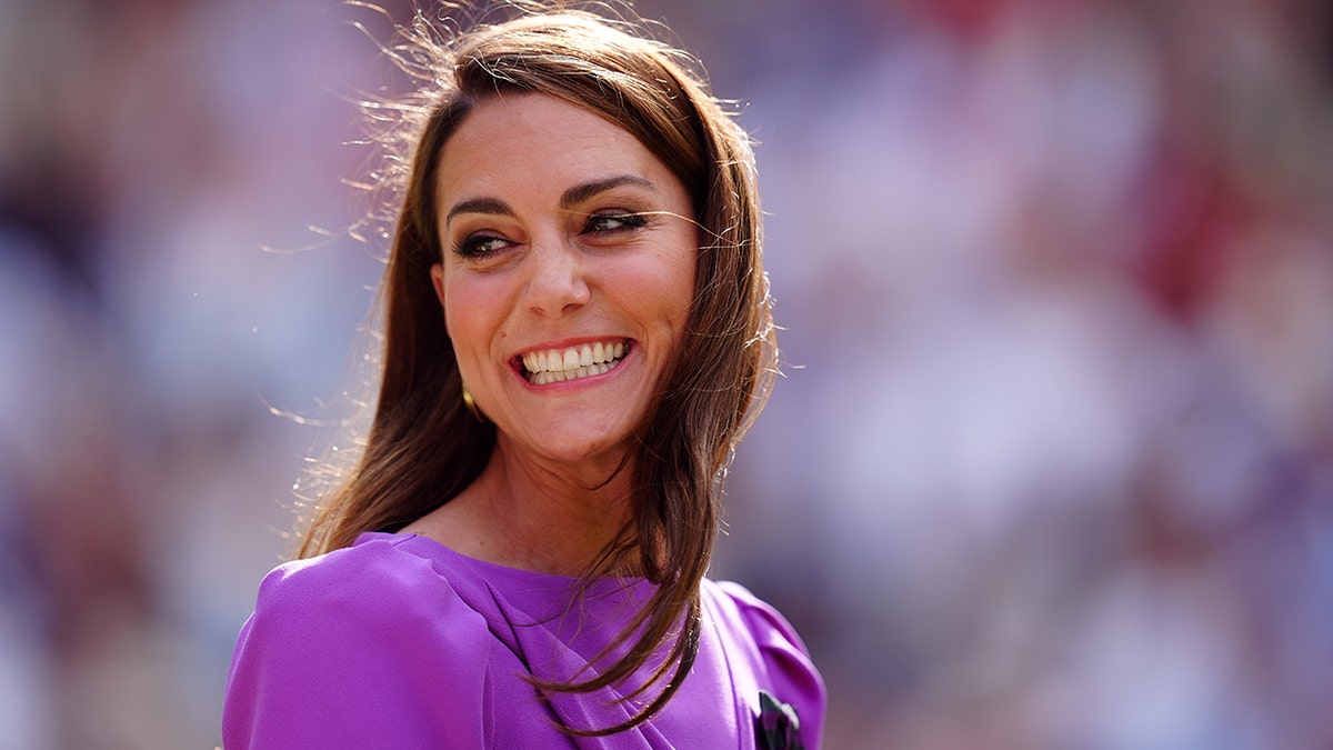 Kate Middleton in a bright purple dress beams and looks to her right at Wimbledon