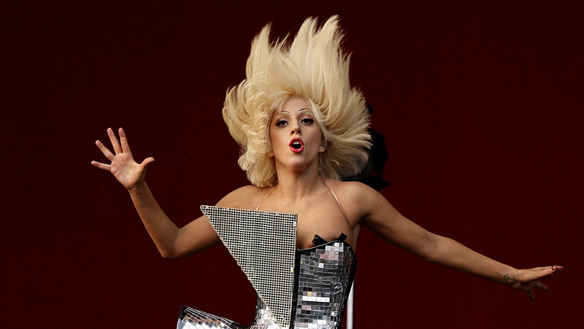 Lady Gaga in an asymmetrical dress that resembles a disco ball rocks out on stage, flipping her head up