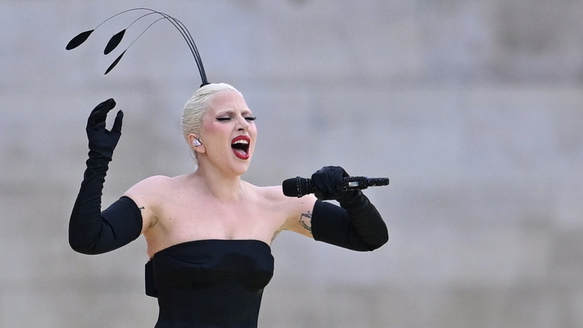 Lady Gaga successful  a strapless achromatic  gown with agelong  achromatic  gloves sings into the microphone passionately with a feather sticking retired  of her hair