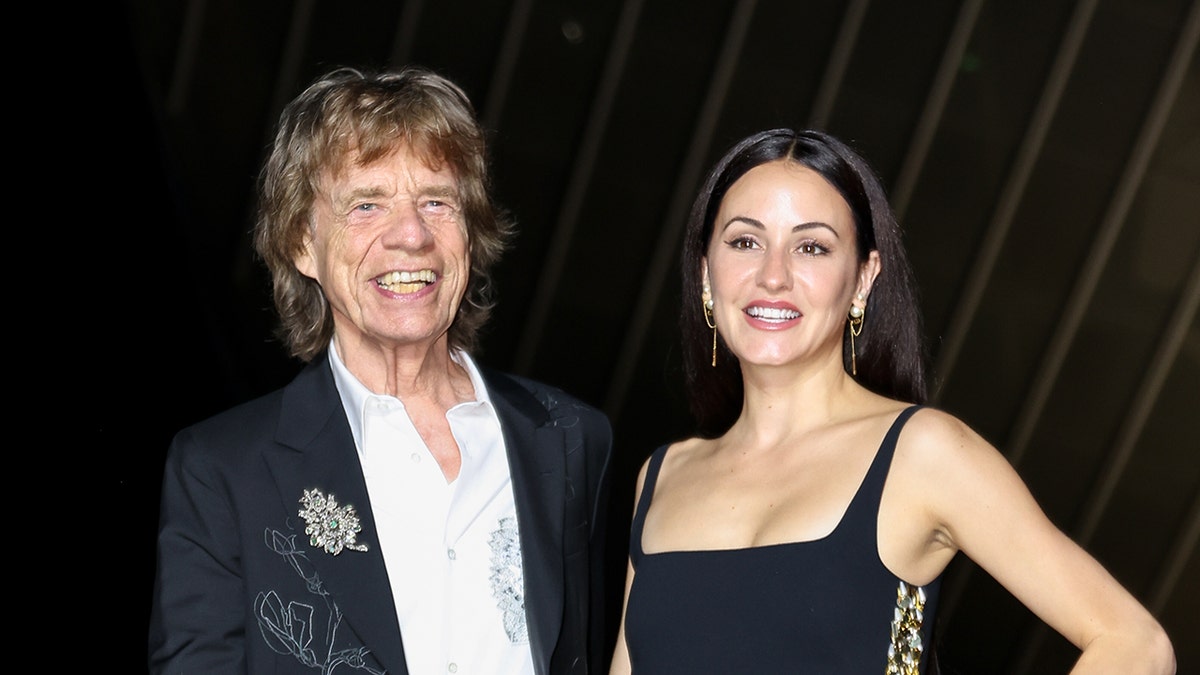 Mick Jagger wears achromatic  suit   with woman  Melanie Hamrock successful  achromatic  dress.