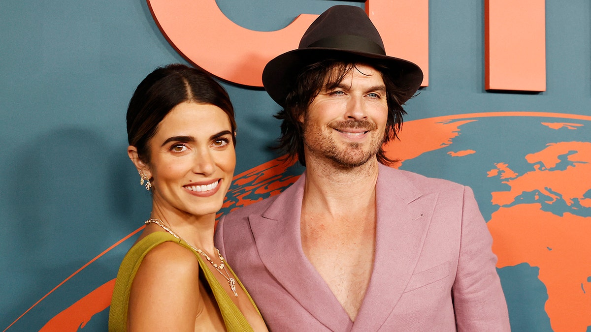 Nikki Reed w zielonej sukience uśmiecha się do kamery z mężem Ianem Somerhalderem w jasnoróżowej marynarce bez koszuli pod spodem i brązowym kapeluszem