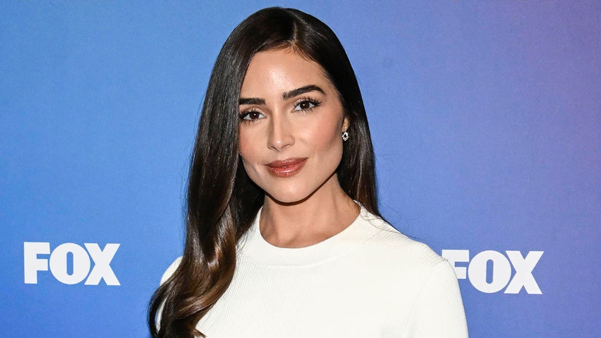 olivia culpo con un vestido blanco de cuello alto y sonriendo en un evento de fox