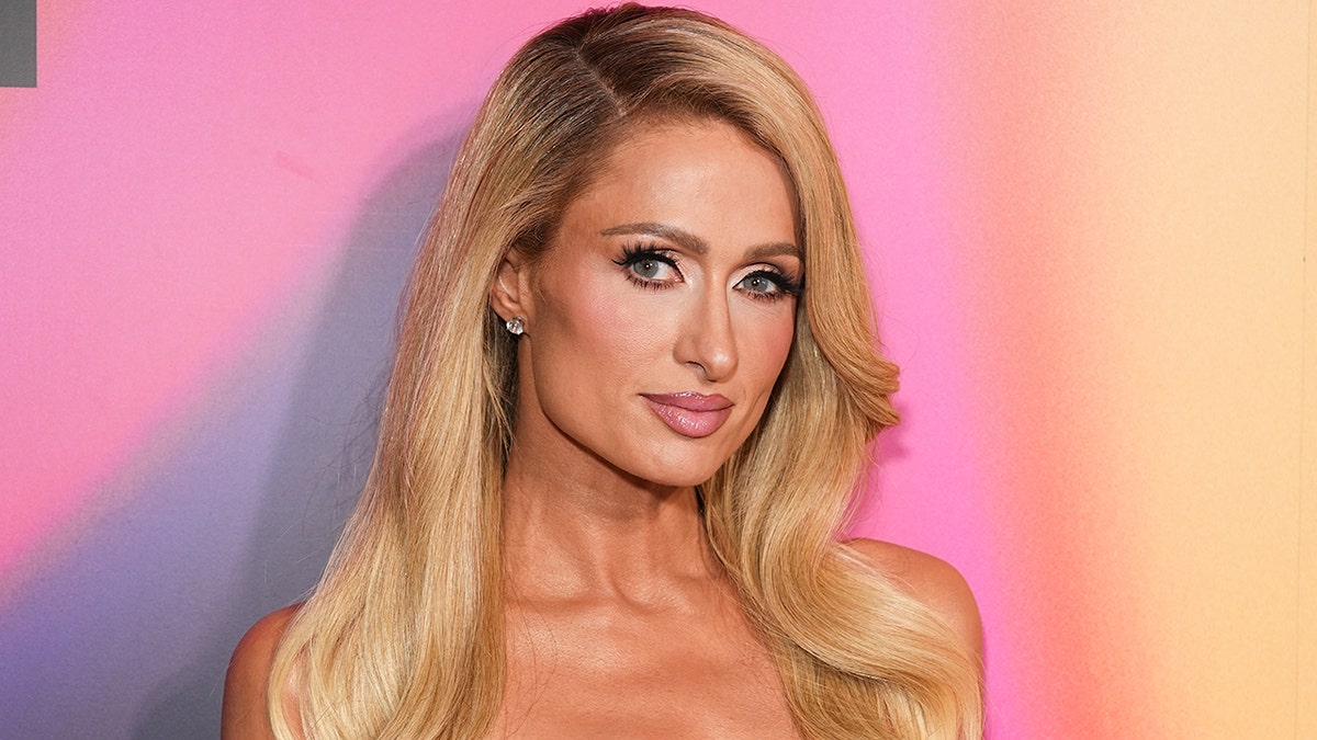 Paris Hilton soft smiles/smirks in a photo against a colorful background