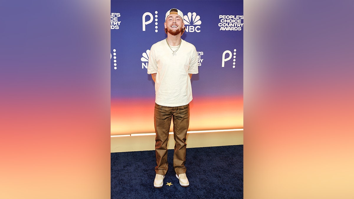 Bailey Zimmerman wears a white shirt and brown pants on the red carpet at the 2024 People's Choice Country Awards.