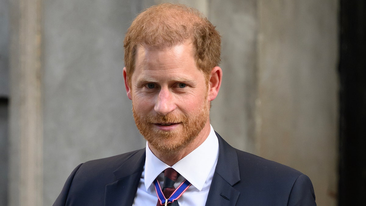 Prince Harry in a navy suit and patterned tie looks slightly away from the camera in London