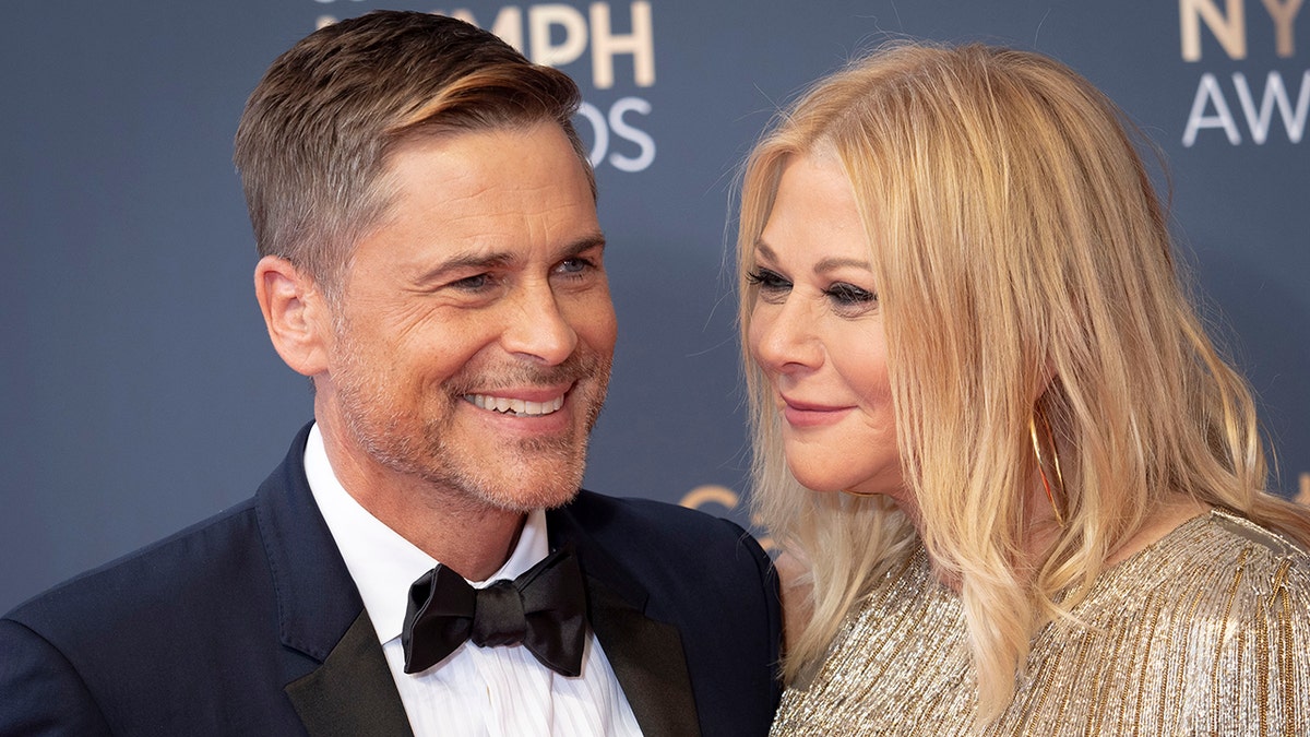 Rob Lowe con esmoquin sonríe mientras su mujer Sheryl con un vestido brillante le mira cariñosamente