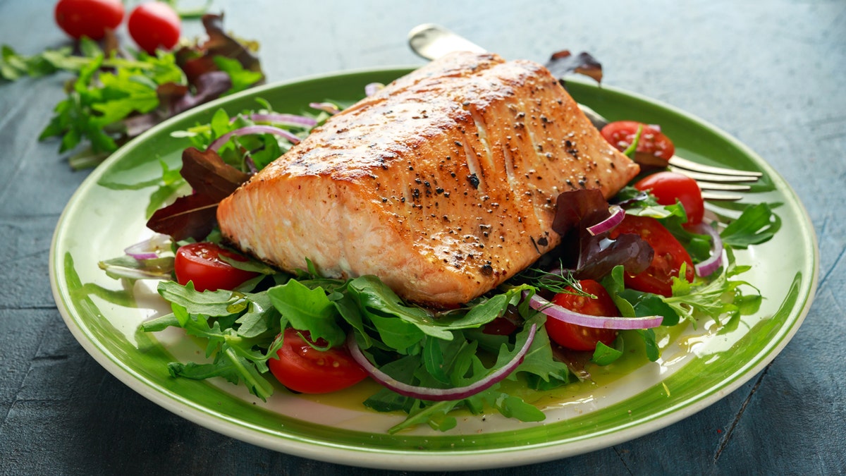 A piece of salmon on top of the salad on a plate.