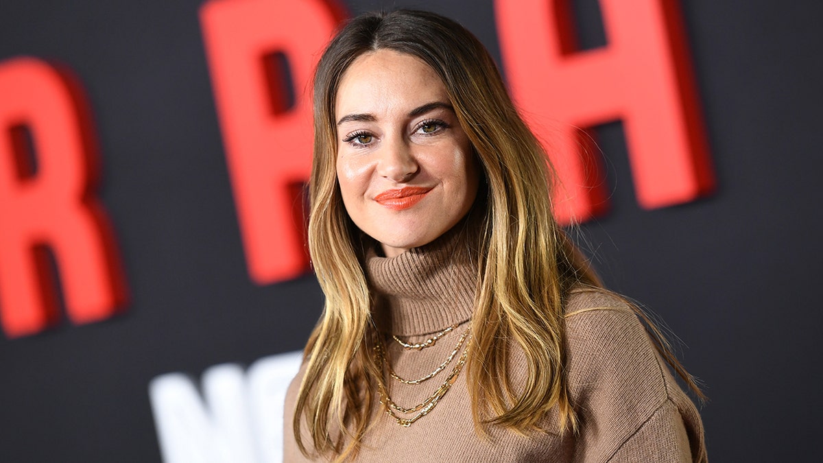 Shailene Woodley con un suave jersey marrón de cuello alto sonríe y mira directamente a la cámara en la alfombra