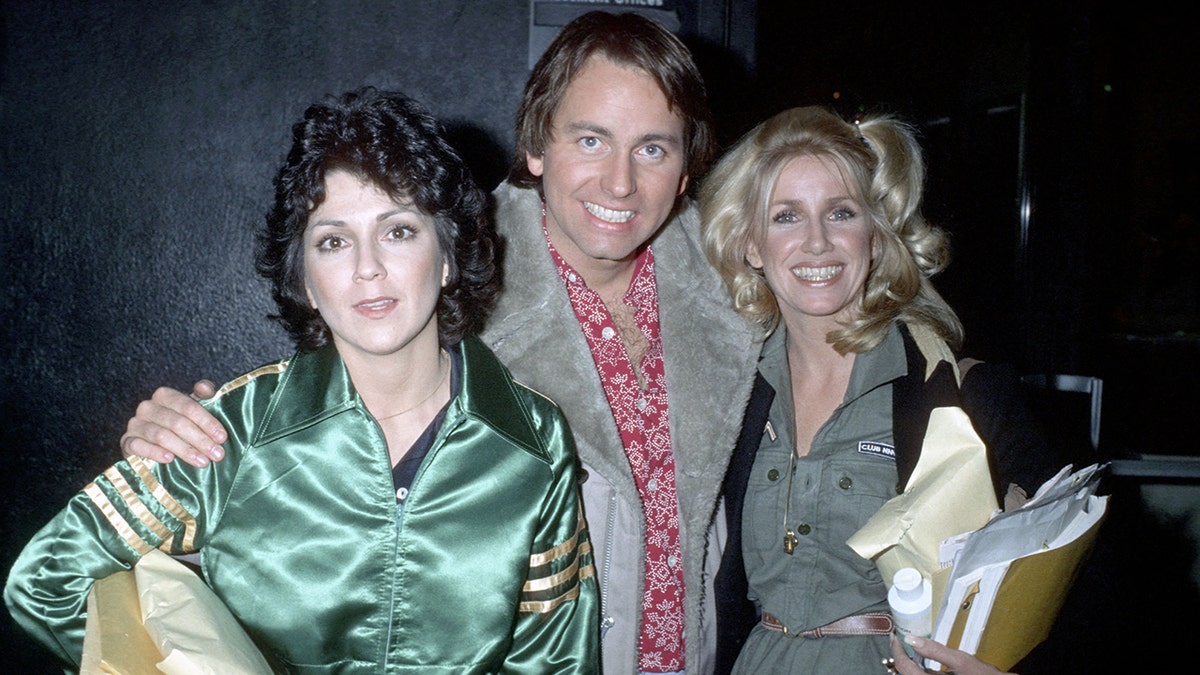 Joyce DeWitt em uma blusa de seda verde é fotografada com um sorridente John Ritter em uma jaqueta de camurça e Suzanne Sommers