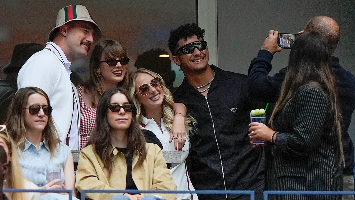 Travis Kelce, Taylor Swift, Brittany Mahomes y Patrick Mahomes sonríen y posan para una foto que se toma en su palco del US Open